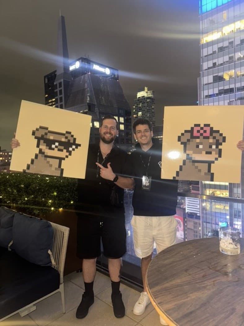 Hayden Harris with Doginal Dogs prints Hayden Harris (@gambitmeta) on a night rooftop holding a Doginal Dogs print beside a friend holding another print